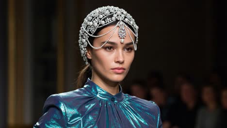a stunning fashion model showcasing a unique jewelry-adorned headpiece and vibrantly colored garment on the runway, captivating the audience with elegance and style