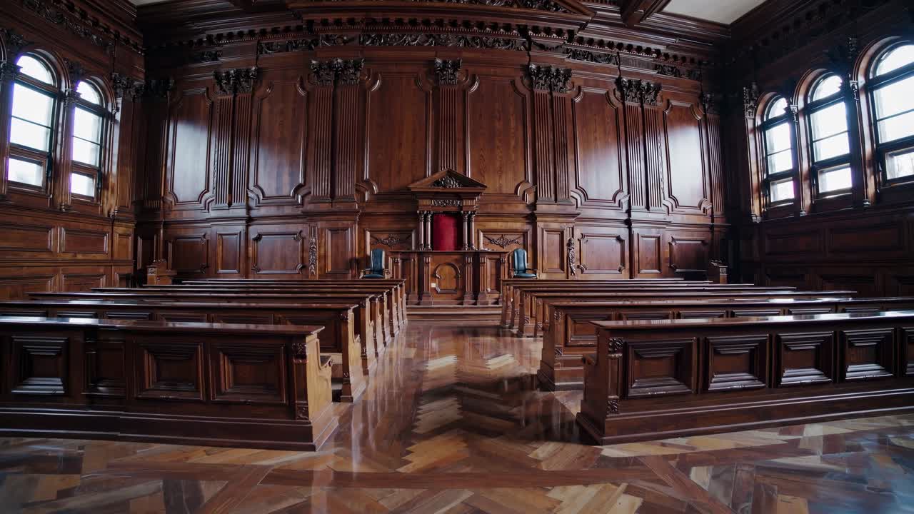 Weitwinkelaufnahme eines verzierten, leeren Gerichtssaals mit Holzinterieur, die eine cineastische, dramatische Atmosphäre einfängt.