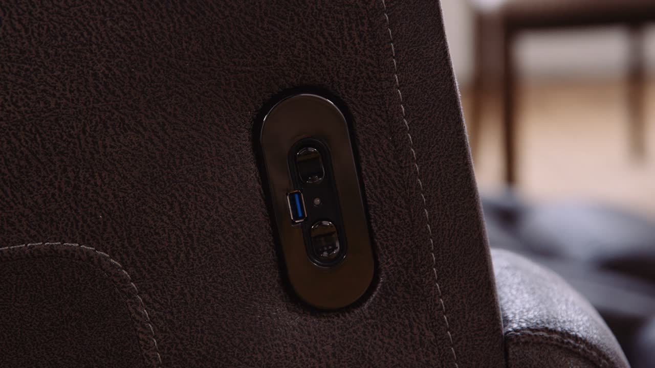 una mano masculina blanca presiona el botón de ajuste de los muebles del hogar en un cargador usb movimiento activado asiento reclinable de potencia sofá de cuero marrón caro en una sala de estar durante el día
