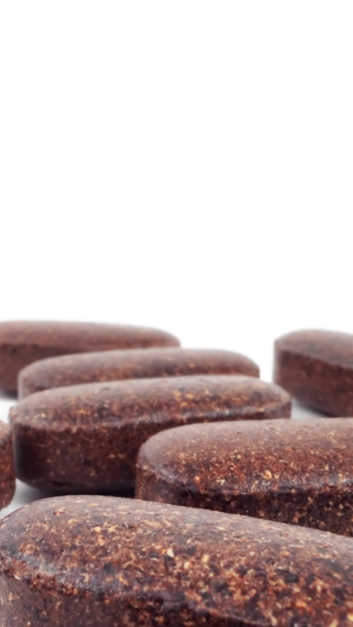 primer plano de comprimidos de suplementos de hierbas marrones esparcidos sobre un fondo blanco