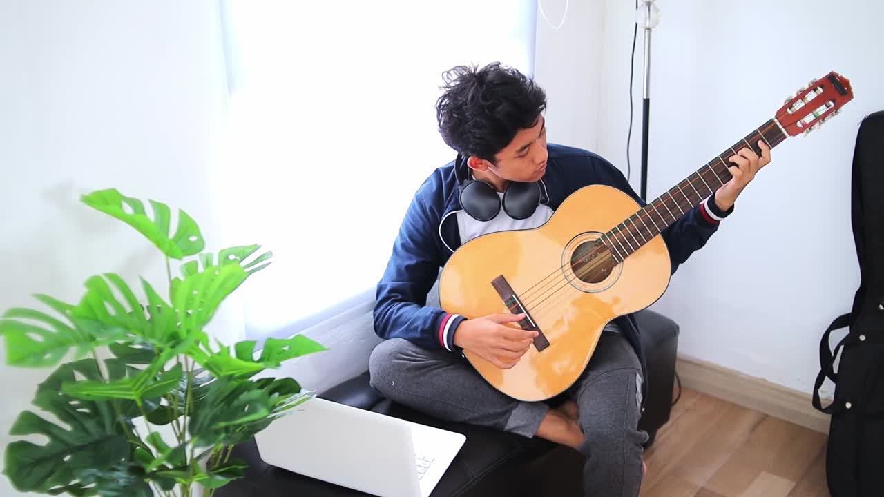Young asian man playing acoustic guitar enjoying creative moment indoors