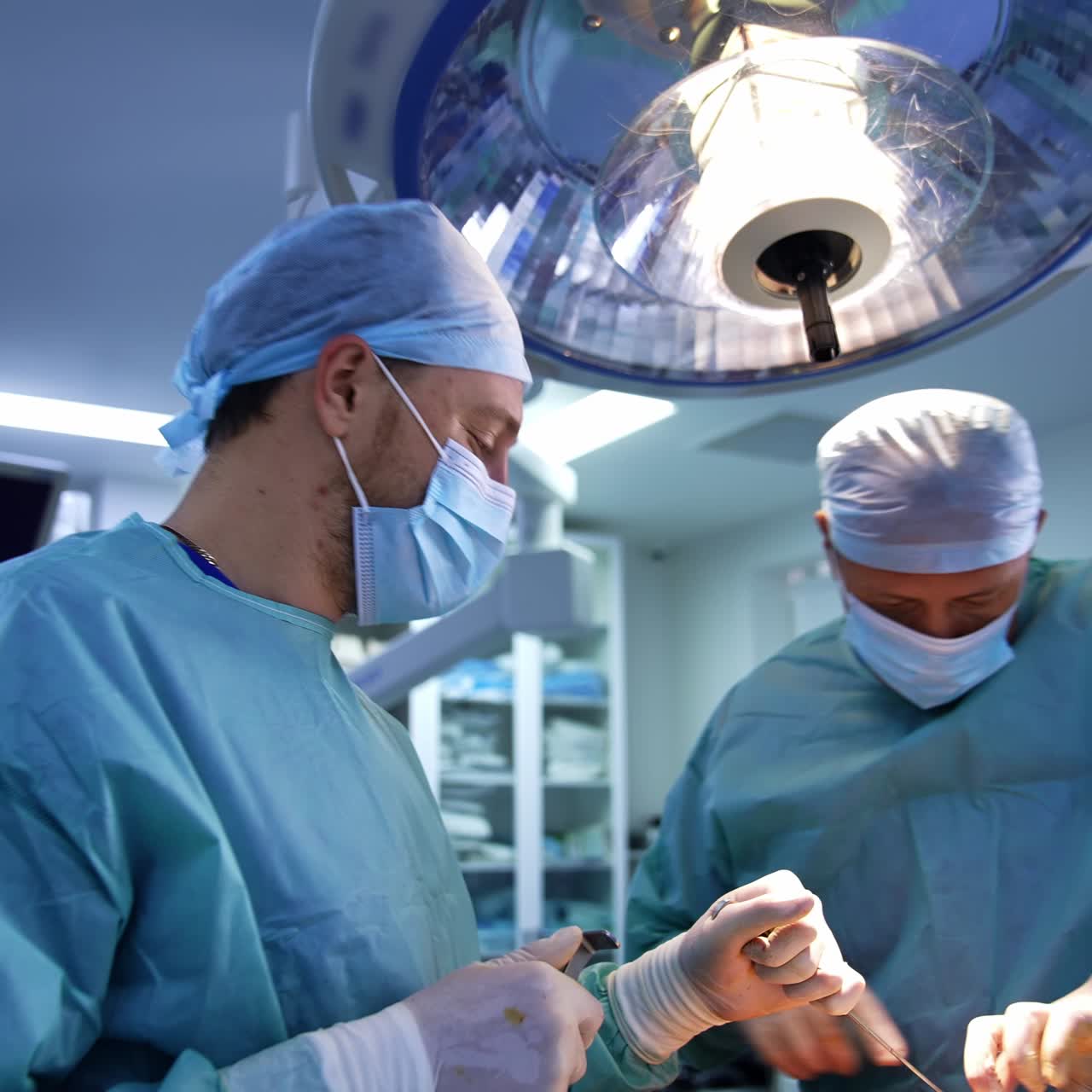 Co-working surgeons use modern tool devices at operation. Female nurse standing behind at backdrop. Blurred background