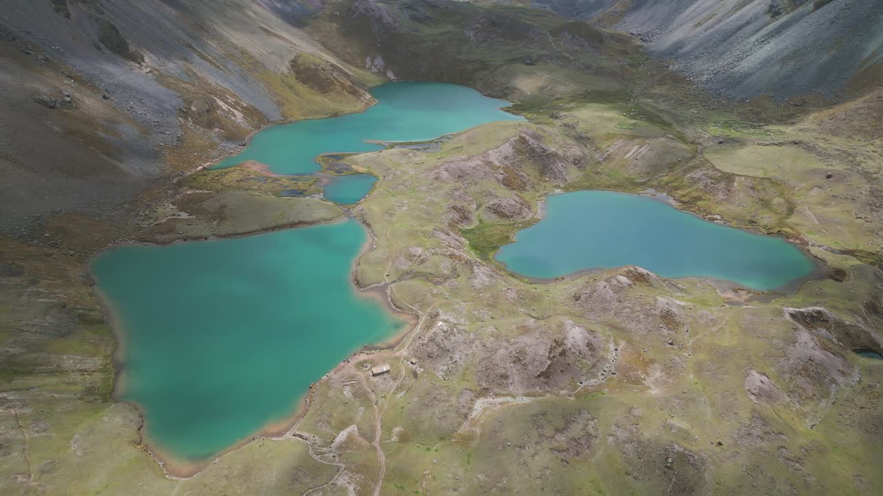 Drone orbit around three turquoise lagoons in Ausangate, with the surrounding mountains and soft light creating a serene and dramatic atmosphere.