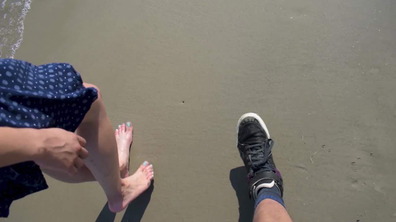 a couple walking on the beach together, she is bare foot and he is wearing shoes, wet sand with waves