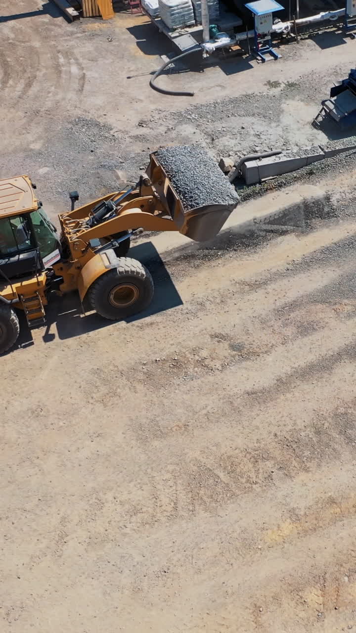 Heavy bulldozer loading sand. Aerial view of machinery and mine equipment near road on sandy surface Vertical video