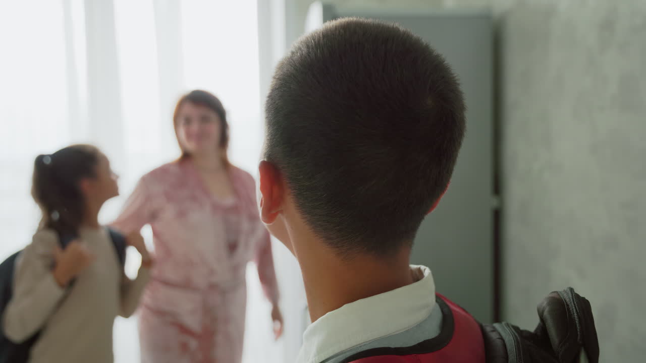 young boy preparing for school adjusting backpack straps in hallway with parent helping behind near closet and window bright natural light morning routine family scene child focus determination
