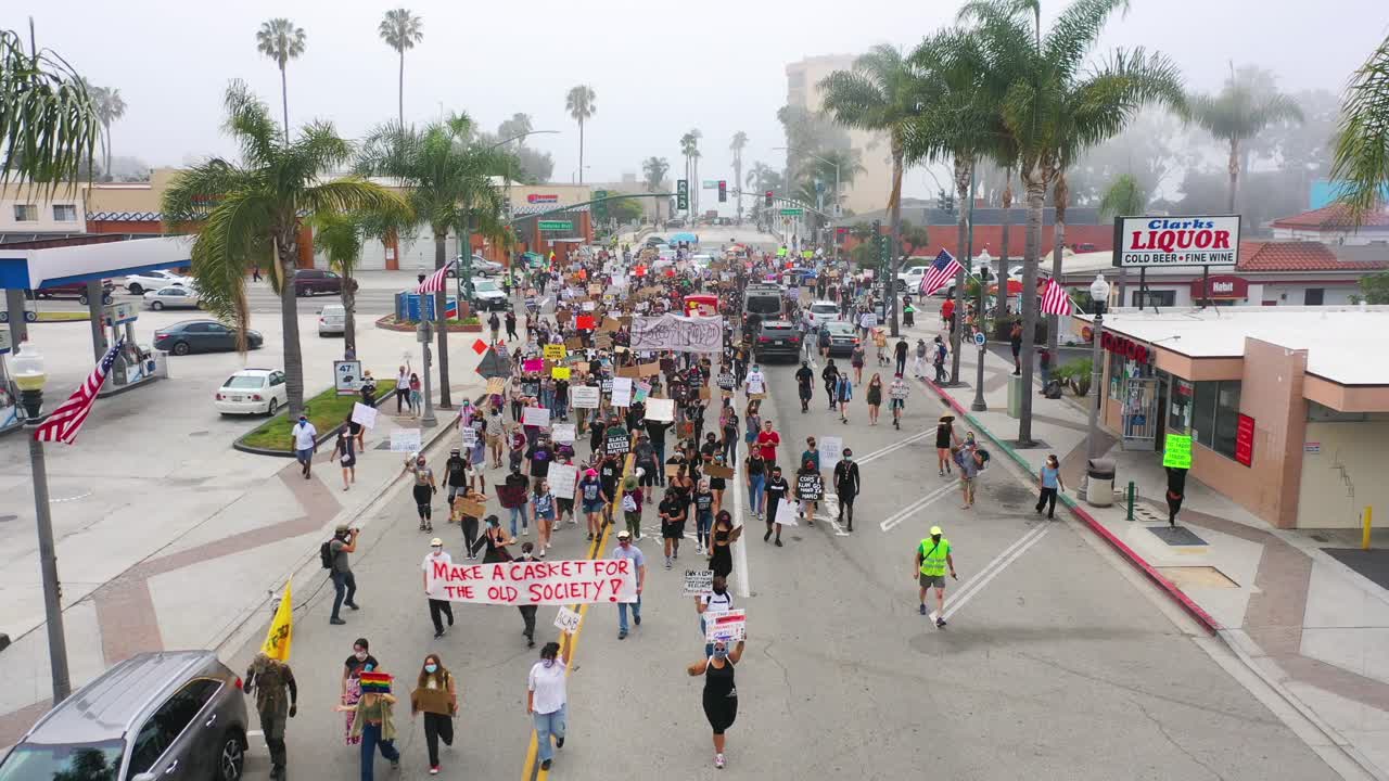 Ottima ripresa aerea su grandi folle in una marcia di protesta Black Lives Matter (BLM) che sfilano attraverso una piccola città, Ventura, California