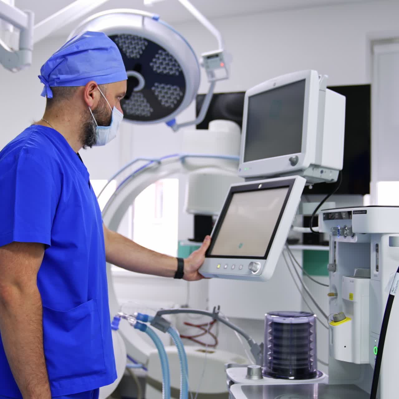 Anesthesiology specialist uniformed and wearing mask standing near modern equipment. Doctor switching on the machine preparing them for surgery