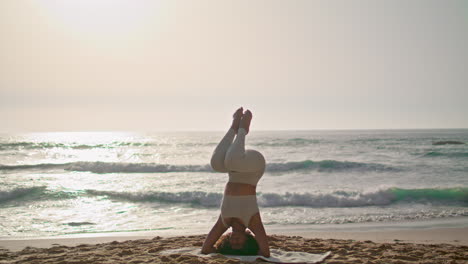 girl practicing lotus headstand at sunrise ursa beach. lady exercising outdoor