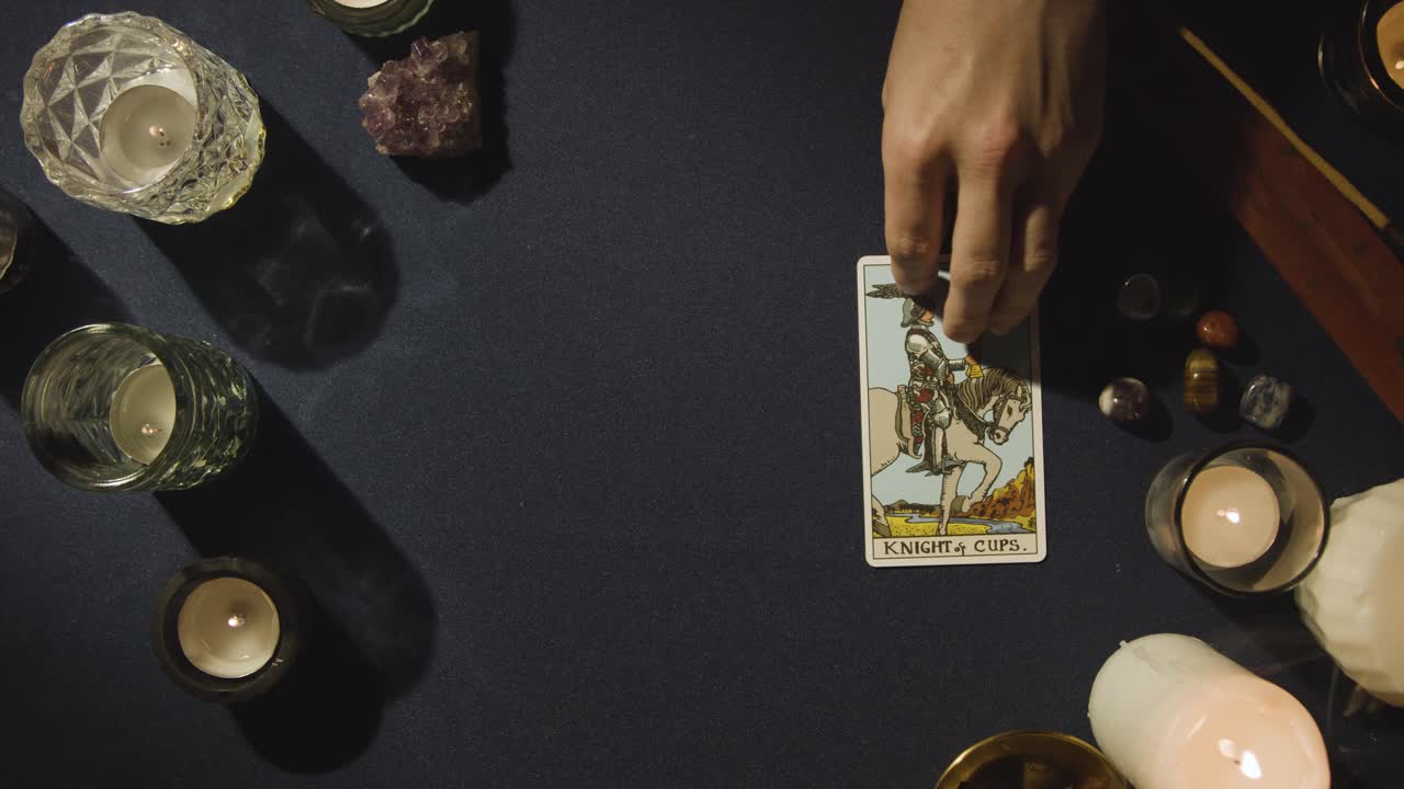 toma aérea de una persona que da una lectura de cartas del tarot colocando la carta del caballero de copas en la mesa 1