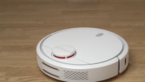 white robotic vacuum cleaner removes debris from the laminate