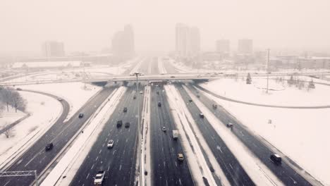 aerial-flying-through-a-national-road-with-heavy-traffic-during-a-snowstorm,-wet-pavement-and-snow-heaped-on-the-sidewalks