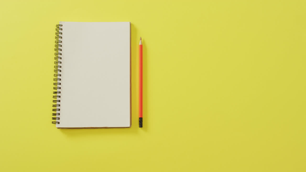 Video of notebook with copy space and pencil on yellow background