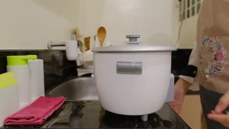 asian housewife moves rice cooker and opens the lid cover in kitchen