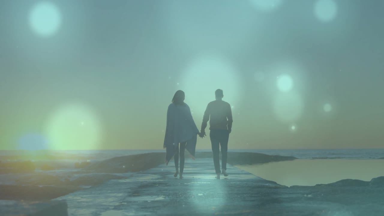 Un couple se tenant la main et marchant sur une jetée au lever du soleil, illustrant le voyage avec des reflets bokeh animés.