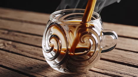 coffee being poured into a unique glass mug on a wooden table