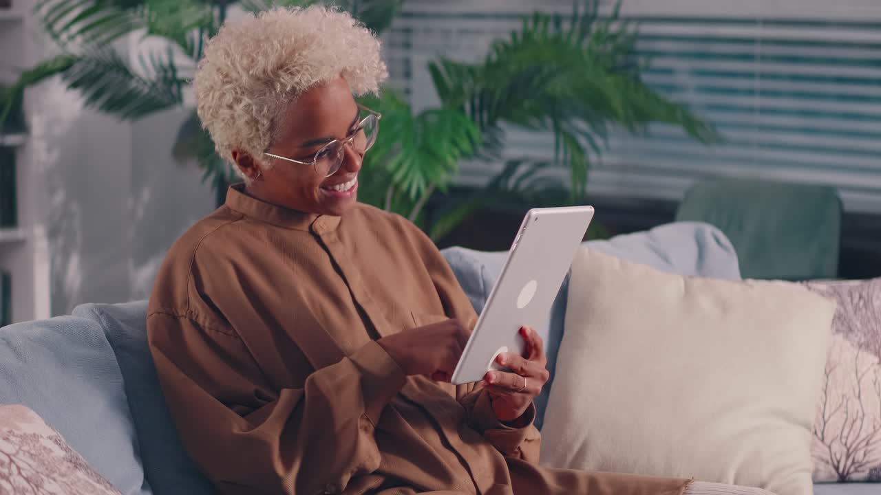 African woman on sofa with digital tablet in hands enjoying social networks