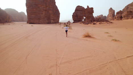 man chasing wild camels running in the sahara desert in tassili n'ajjer national park during sunset in africa