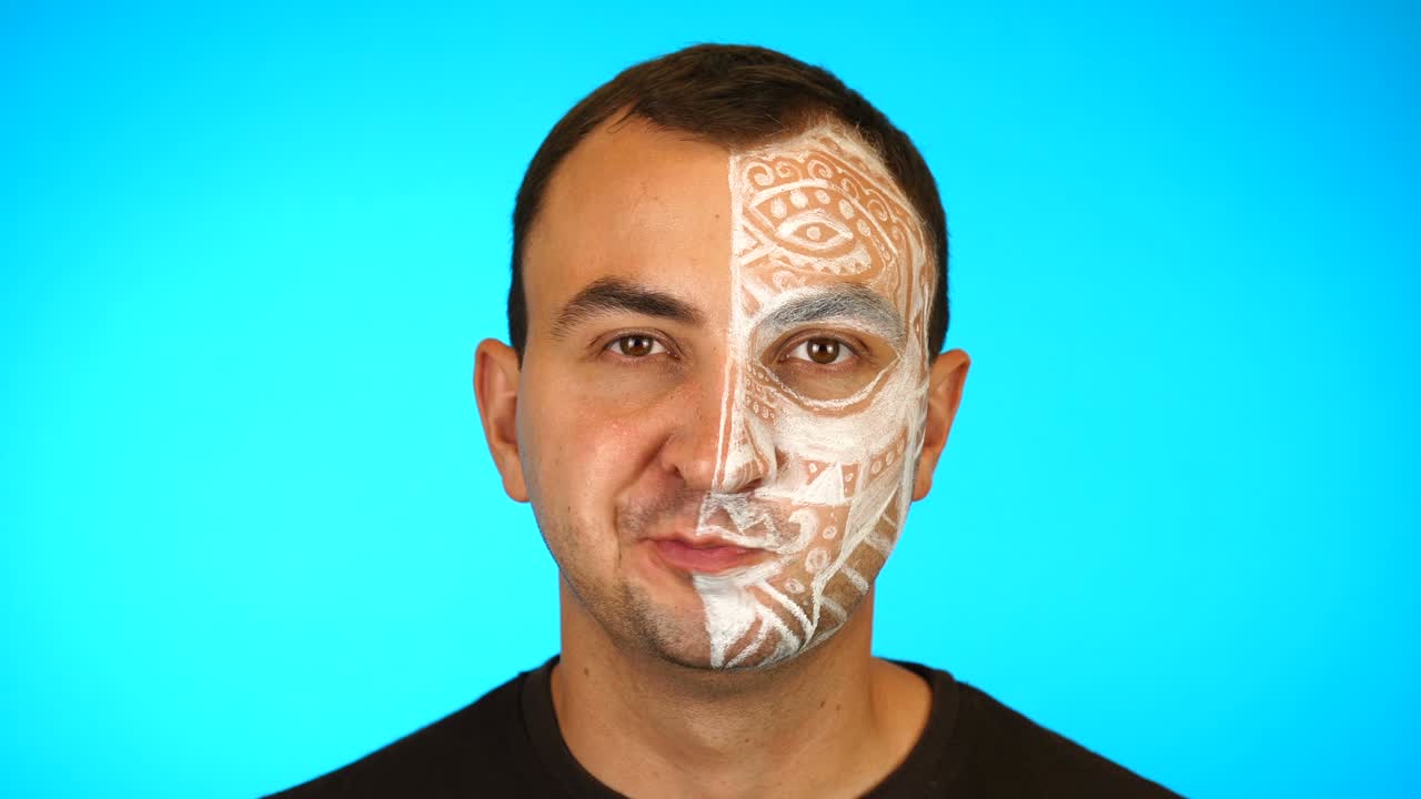 hombre pintado mirando a la cámara y masticando contra un fondo azul