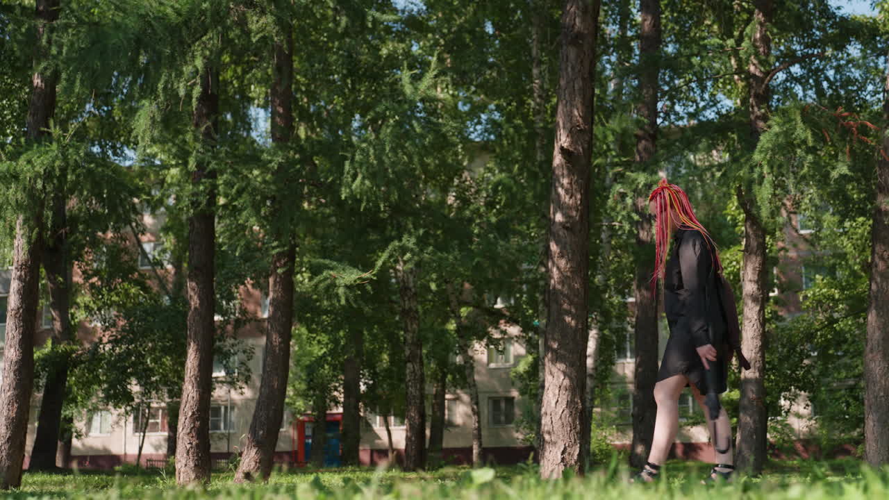 Молодая уверенная в себе женщина в модной городской одежде демонстрирует стильный образ на фоне листвы в городской среде. Яркая сцена, запечатлевшая уверенную походку стильной девушки по зеленому городскому парку.