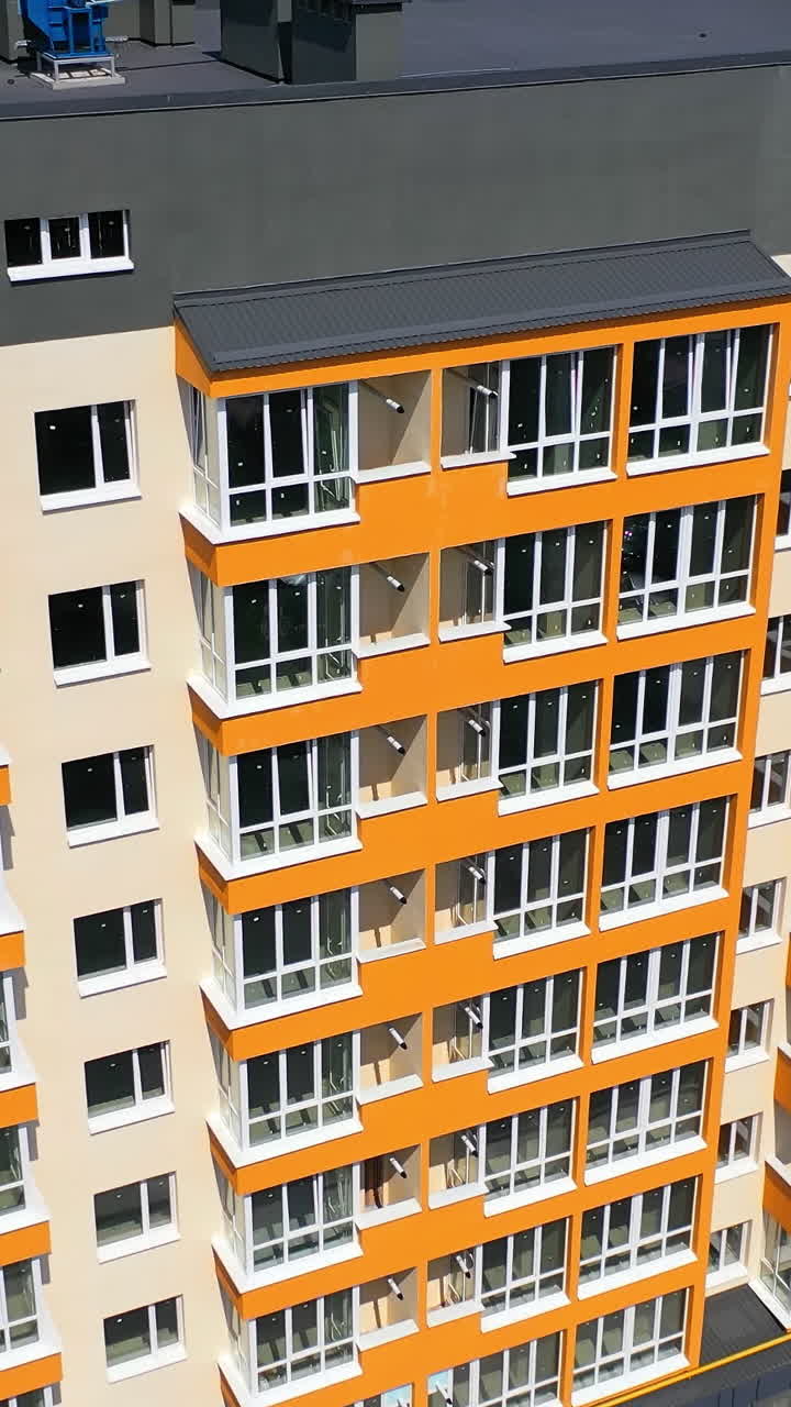 New high-rise building of modern design. Multi storey building with large covered balconies in orange color. Motion camera down. Vertical video