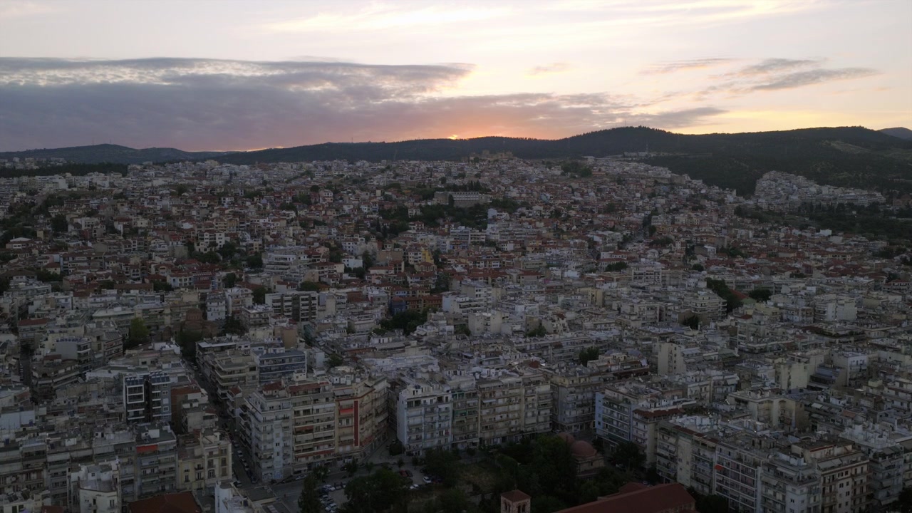 Vista aerea all'alba con drone di Salonicco, Grecia, che mostra un denso paesaggio urbano collinare di edifici bianchi e color terracotta che si estendono verso montagne distanti
