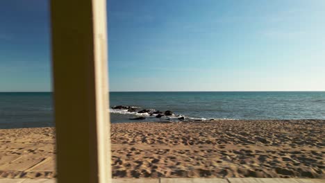 Die-Küste-Beobachtend,-Sich-Seitwärts-Hinter-Strandhaussäulen-Bewegend