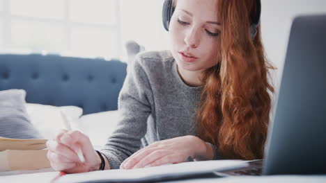 estudiante universitaria que usa auriculares trabaja en la cama en una casa compartida con portátil y teléfono móvil