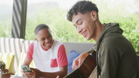 Happy-diverse-male-teenage-friends-playing-guitar-at-home,-slow-motion