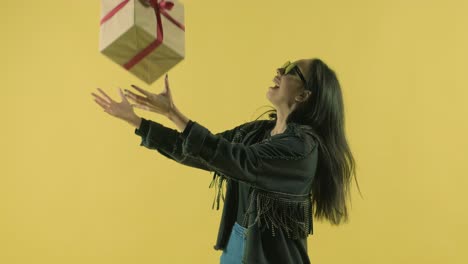 chica feliz con una caja de regalos y mirando a la cámara sobre un fondo amarillo