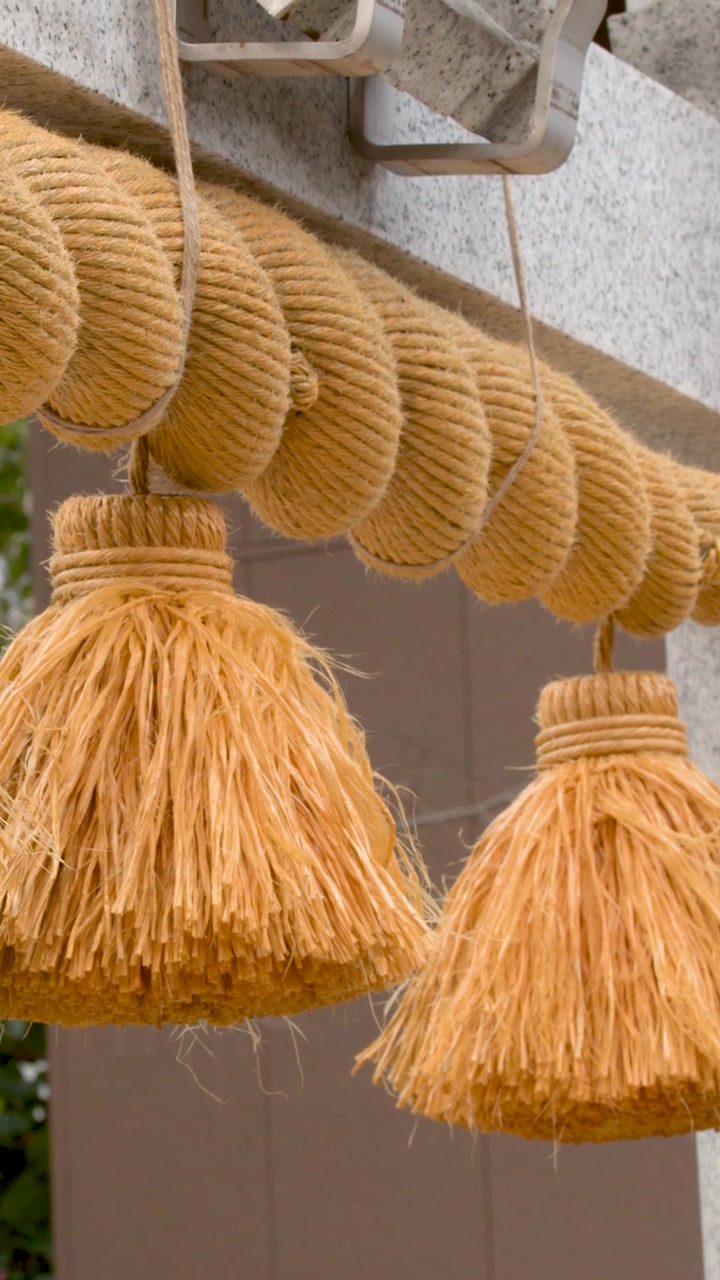 Primo piano di una spessa corda shimenawa con nappe pendenti da un torii di pietra.