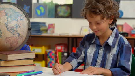 vista frontal de un escolar caucásico estudiando en el escritorio en el aula de la escuela 4k