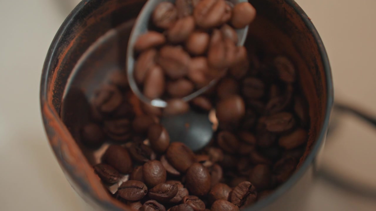 Chicchi tostati si versano nella tazza. Rituale mattutino della preparazione del caffè fresco. Tazza di metallo rustica riempita di chicchi tostati aromatici. Scatto intimo di chicchi di caffè caldi versati con un cucchiaio in una tazza di metallo invecchiato.