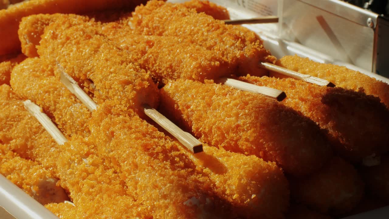 Cooking corn dogs in boiling oil close-up. Traditional asian corndog snacks street food. Fried sausage in breadcrumbs on a stick. Korean Chinese street local market with traditional food. American fast food corndogs with sauce on the top. High quality 4k footage