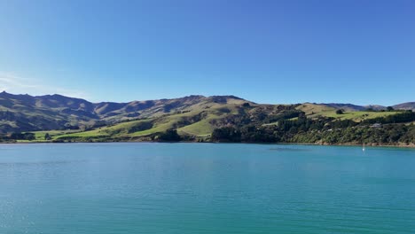 aerial footage captures akaroa's serene lake and rolling hills under clear blue skies, showcasing natural beauty and tranquility