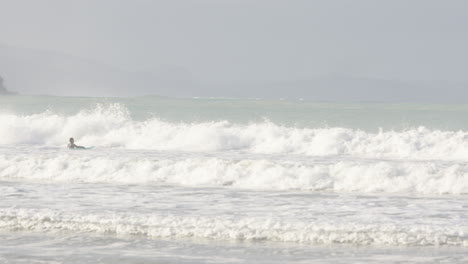 Wide-shot-of-a-surfer-swimming-out-in-the-sea-in-Castle-Point,-New-Zealand