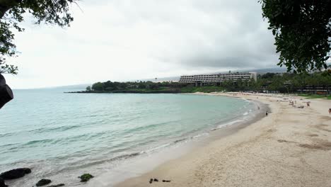 mauna kea beach on the big island of hawaii with a view of the ocean and a resort hotel in the distance - ascending crane shot framed by trees