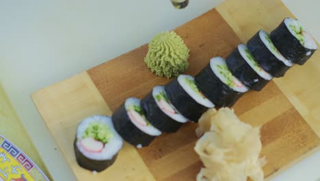 close up for chef hands in cooking gloves squeezing green wasabi sauce on a plate for prepared rolls