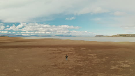 adventurous explorer discovering the patagonian steppe near el calafate, santa cruz, argentina.
aerial back view of lona man walking toward the lake in the vastness of the steppe.