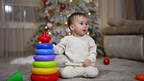toddler playing with stacking rings by christmas tree