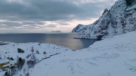 Vista-Aérea-Del-Paisaje-Montañoso-De-Las-Islas-Lofoten-Cubiertas-De-Nieve-Avanzando-Hacia-La-Costa-Del-Océano-Azul