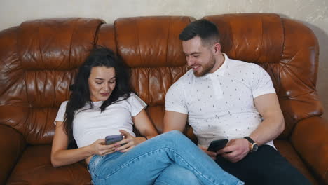 couple in love spend time together. beautiful woman and man sitting on a comfortable couch and using phones at home.