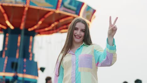 beautiful young caucasian girl showing victory sign by hands outside in a amusement park while wearing vibrating coulours