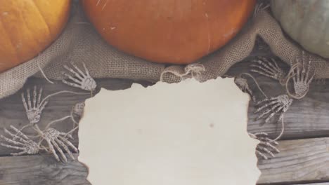 paper with copy space against skeleton hands and pumpkins on wooden surface