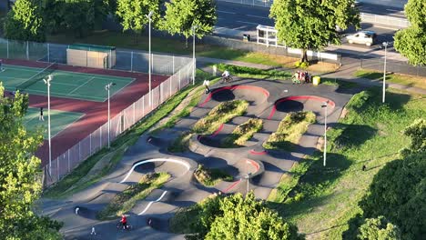 Jugendliche-Auf-Rollern-Und-Mountainbikes-Fahren-An-Einem-Sonnigen-Sommertag-Auf-Einem-Hügeligen-Skatepark-Neben-Den-Tennisplätzen-Im-Hillsborough-Park-In-Sheffield