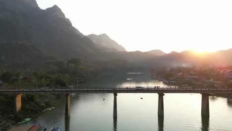 drone-shot-of-sunset-behind-the-bridge-in-the-mountain-town-of-Nong-Khiaw-in-Laos,-Southeast-Asia