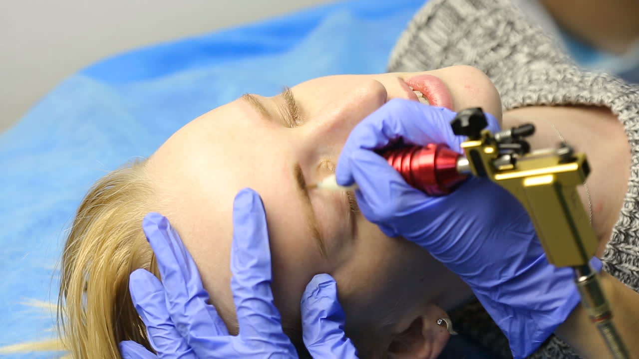 Beautician hands doing eyebrow tattoo on woman face