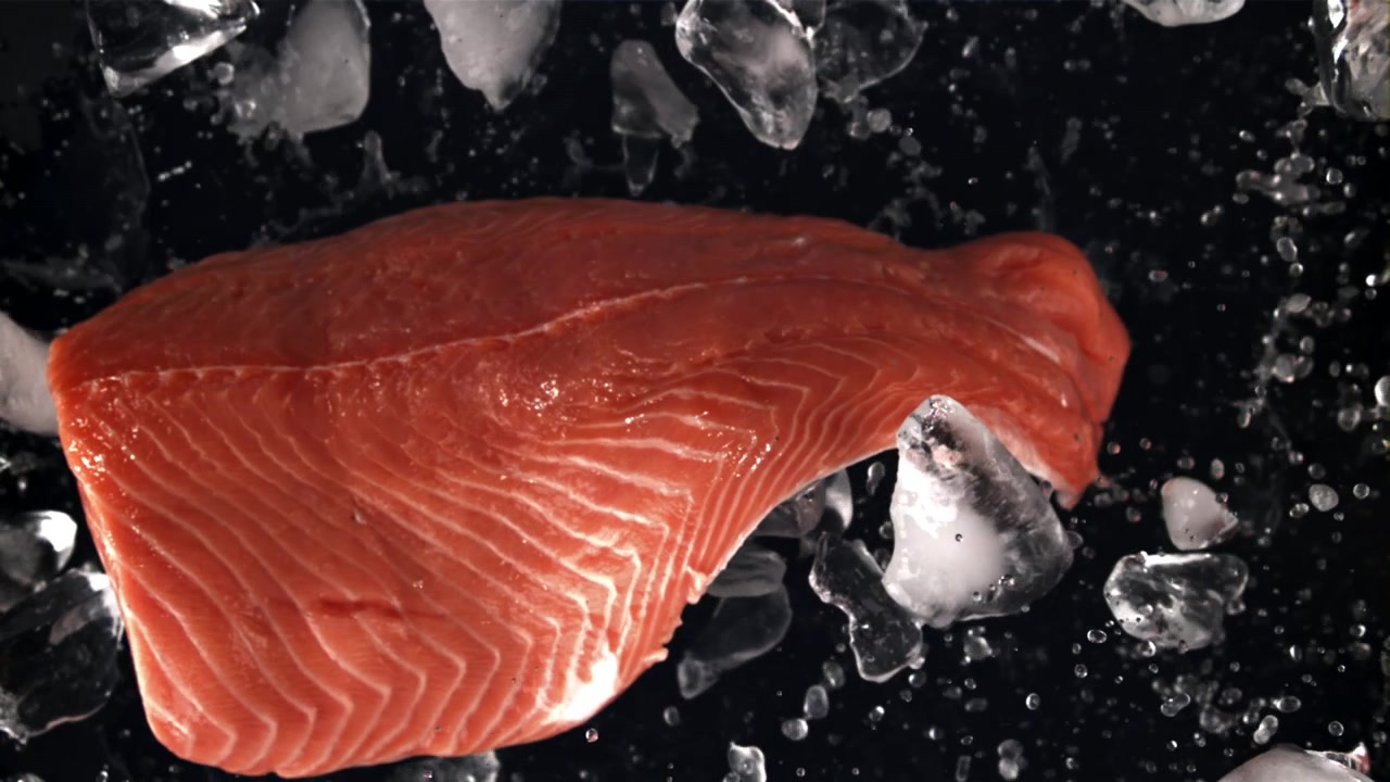 Filetto di salmone fresco crudo con ghiaccio che schizza su sfondo nero