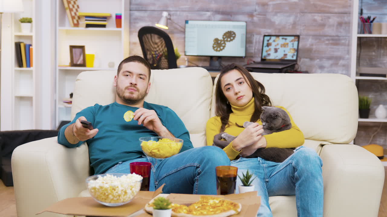 Coppia che guarda la TV con il proprio gatto e si gusta degli snack