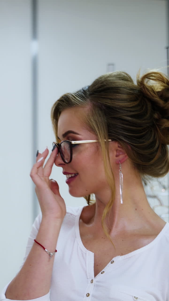 Elegant woman wearing new eyeglasses at optic store. Beautiful young model trying on modern glasses in the shop. Vision concept. Vertical video